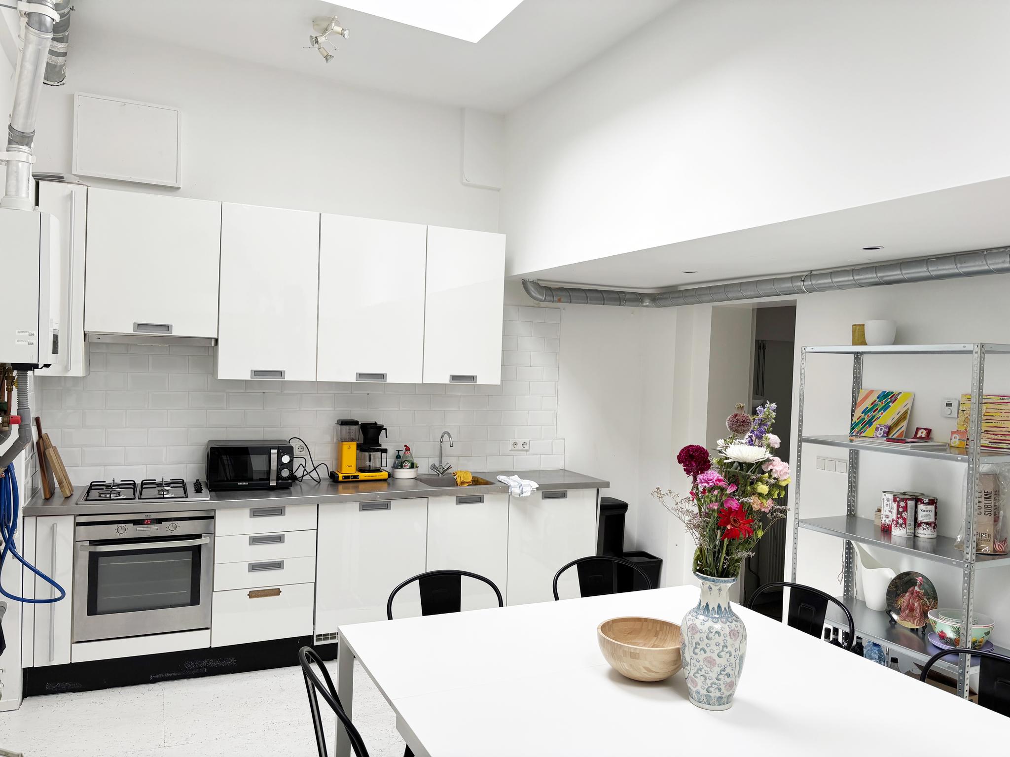 Moderne witte keuken aan de Van Ostadestraat met eettafel, bloemenvaas en open wandrek.